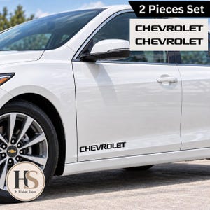 Könnte beinhalten: Ein zweiteiliges Set aus schwarzen Vinyl-Aufklebern mit dem Schriftzug CHEVROLET in einer fetten, serifenlosen Schriftart. Die Aufkleber sind für die Anbringung an den unteren Seitenverkleidungen eines weißen Fahrzeugs vorgesehen.
