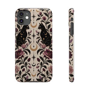 May include: A mobile phone case featuring a repeating pattern of black cats, dark purple roses, and gold crescent moons on a cream background. The design includes vertical lines with star accents and foliage, shown from both front and side angles.