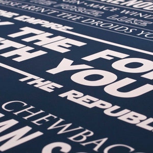 May include: A navy blue poster with white text that reads "May the Force be with you" and "The Republic". The poster also includes the names of characters from the Star Wars franchise, including "Luke", "Han", "Chewbacca", and "Obi-Wan Kenobi".
