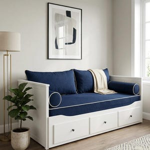 Peut inclure: Un lit de repos blanc doté de trois tiroirs de rangement, comprenant un matelas rembourré bleu foncé, deux coussins traversins assortis et deux coussins de dossier rectangulaires, le tout rehaussé d'un passepoil blanc. Un plaid crème est posé dessus.
