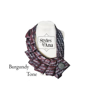 May include: Burgundy tone tie necklace with a silver button closure. The necklace is made from a patterned tie and is styled in a ruffled fashion. The label "Styles by Ana" is visible in the center of the image.