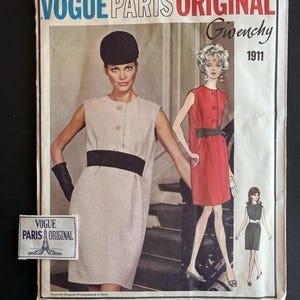 May include: A Vogue Paris Original Givenchy sewing pattern envelope 1911 featuring a sleeveless shift dress with a wide waistband and button front. The cover displays a beige dress, a red dress, and a black dress illustration with a small fabric label.