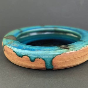 May include: A round ceramic dish with a teal blue glaze that has dripped down the sides. The dish has a brown clay base.