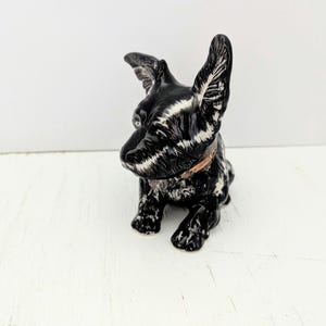 May include: A black and white ceramic dog ornament with large, upright ears and a brown collar. The dog is sitting on a white surface. The ornament has a glossy finish and detailed features.