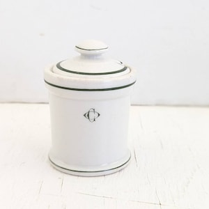 May include: White ceramic jar with a green lid and a green band around the top and bottom. The jar has a black letter "C" monogram.