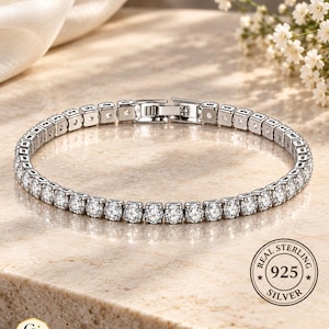 Könnte beinhalten: Ein silberfarbenes Tennisarmband mit einer durchgehenden Reihe runder, klarer, facettierter Steine in einer Metallfassung. Das Armband verfügt über einen sicheren Verschluss und einen runden Stempel mit der Aufschrift REAL STERLING 925 SILVER.