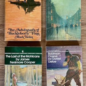 May include: Four vintage paperback books are displayed. Titles include "The Adventures of Huckleberry Finn," "Dr. Jekyll and Mr. Hyde," "The Last of the Mohicans," and "Robinson Crusoe." Each book features unique cover art, with illustrations and text.