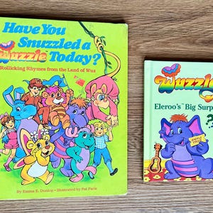 May include: Two children's books with colorful illustrations. The larger book is titled "Have You Snuzzled a Wuzzle Today?" and the smaller book is "Wuzzles Eleroo's Big Surprise". Both books feature cartoon characters.
