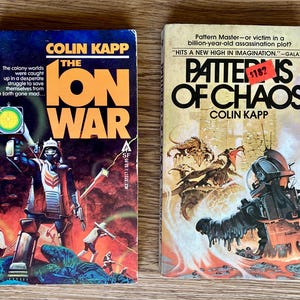 May include: Two paperback science fiction books by Colin Kapp. The book on the left is titled "The Ion War" and features a futuristic scene with a soldier in a red and white suit. The book on the right is titled "Patterns of Chaos" and features a futuristic scene with a creature in a black and silver suit.