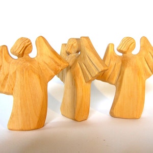 May include: Three wooden angel figurines with outstretched wings. The angels are carved from light brown wood and have a simple, rustic design.