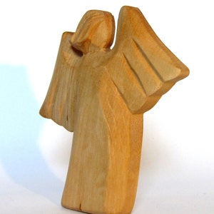 May include: A wooden angel figurine with outstretched wings. The angel is carved from light brown wood and has a simple, elegant design.