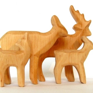 May include: A set of four wooden deer figurines, carved in a simple style. The deer are all facing the same direction, with the largest deer in the back and the smallest deer in the front. The deer are all a light brown color.