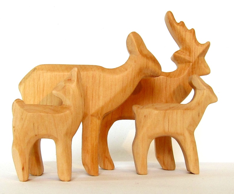 May include: A set of four wooden deer figurines, carved in a simple style. The deer are all facing the same direction, with the largest deer in the back and the smallest deer in the front. The deer are all a light brown color.