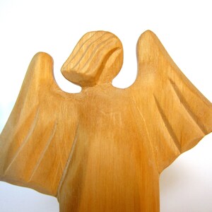 May include: A wooden angel figurine with outstretched wings. The angel is carved from light brown wood and has a simple, elegant design.