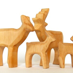May include: A set of four wooden deer figurines, carved in a simple, rustic style. The deer are all different sizes, with the largest deer having antlers. The deer are all made of light brown wood.
