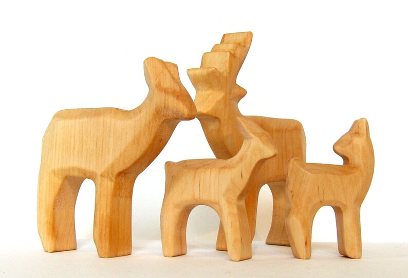 May include: A set of four wooden deer figurines, carved in a simple, rustic style. The deer are all different sizes, with the largest deer having antlers. The deer are all made of light brown wood.