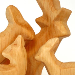May include: Three wooden animal figurines, a deer, a rabbit, and a fox, are carved in a light brown color. The figurines are arranged in a group, with the deer standing in the center.