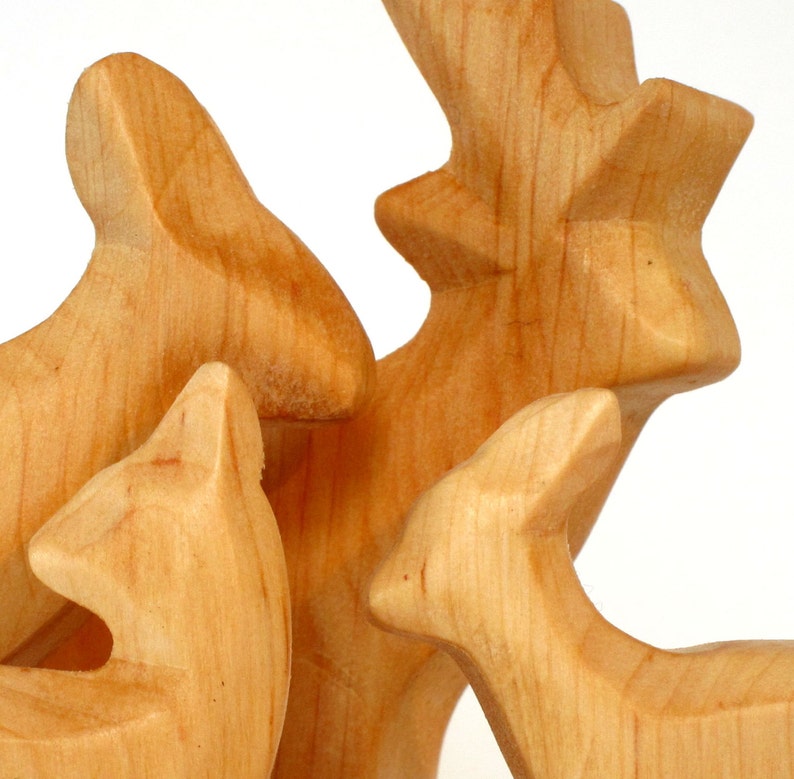 May include: Three wooden animal figurines, a deer, a rabbit, and a fox, are carved in a light brown color. The figurines are arranged in a group, with the deer standing in the center.