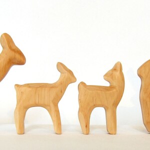 May include: A set of four wooden deer figurines, including a buck with antlers, a doe, and two fawns. The figurines are all carved from light brown wood and have a natural finish.