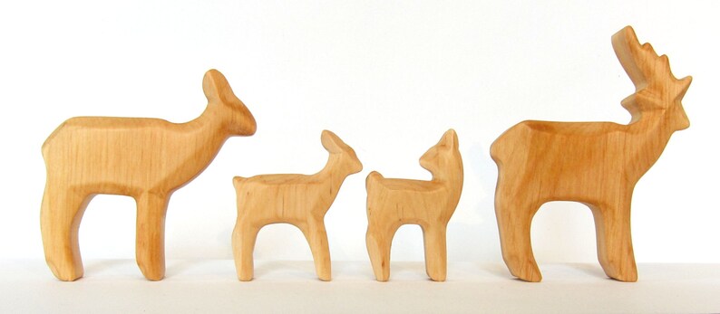 May include: A set of four wooden deer figurines, including a buck with antlers, a doe, and two fawns. The figurines are all carved from light brown wood and have a natural finish.