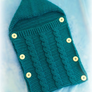 Può includere: Un sacco a pelo per neonati in maglia blu turchese con cappuccio e bottoni bianchi.