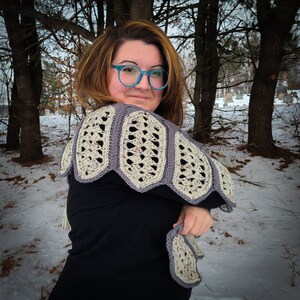May include: A woman wearing a black top with a crocheted shawl in shades of grey and white. The shawl has a scalloped edge and a geometric pattern.