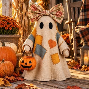 May include: A beige fabric ghost figurine featuring black oval eyes, a large floral print bow on top, and various colorful fabric patches sewn onto the body. The ghost holds a small orange felt jack-o'-lantern bucket with a dark handle.