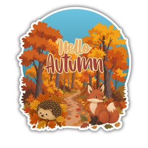 May include: A die-cut sticker featuring a forest scene with orange and yellow autumn leaves, a path, a hedgehog, and a fox. The text "Hello Autumn" is printed in the center in a light brown script font against a blue sky background.