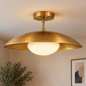 Könnte beinhalten: Eine halb-bündige Deckenleuchte mit einem breiten, gebürsteten Messing-Kuppelschirm mit perforiertem Rand. Unter dem Metallschirm befindet sich eine zentrale, kugelförmige weiße Glaskugel, die an einem runden Messing-Deckenbaldachin befestigt ist.