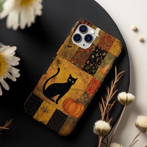 Op de afbeelding: Een smartphonehoesje met een patchworkontwerp met diverse herfstpatronen in oranje, bruine en zwarte tinten. De centrale afbeelding toont een zwarte kat die naast een oranje pompoen op een getextureerde achtergrond zit.