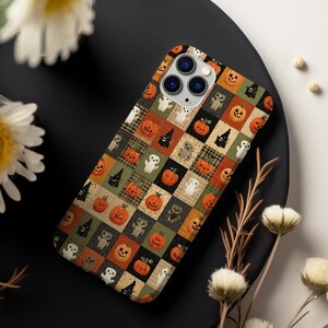 May include: A smartphone case featuring a repeating grid pattern of Halloween-themed illustrations. The design includes orange pumpkins, white ghosts, black witch hats, and small grey creatures arranged in alternating squares of orange, green, and beige.