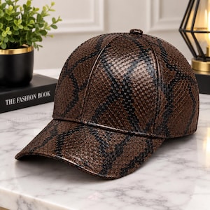 May include: A baseball cap featuring a brown and black snakeskin pattern with a textured, glossy finish. The cap has a structured crown, a curved brim, and a small button at the top centre, showcasing a detailed reptilian scale design.