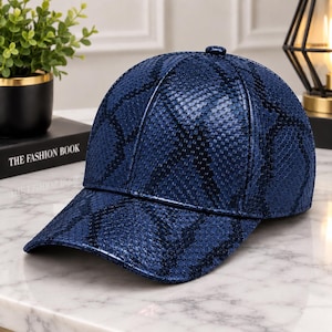 May include: A baseball cap in a deep navy blue colour featuring a textured snakeskin pattern across the entire surface. The cap has a structured crown, a curved brim, and a small button at the top centre, showcasing a glossy and reflective finish.