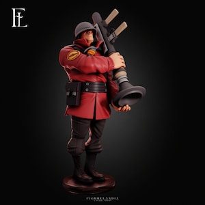 Peut inclure: Une figurine de collection représentant un soldat vêtu d'une veste rouge, d'un pantalon sombre et d'un casque gris. Le soldat tient un grand lance-roquettes gris sur l'épaule. La figurine repose sur une base circulaire avec le texte FIGURELANDIA COLLECTIONS.
