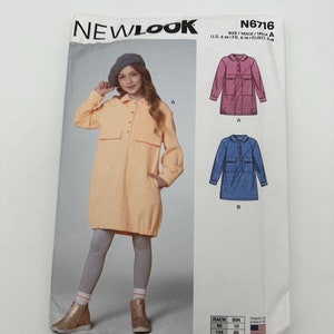 May include: A New Look sewing pattern, N6716, featuring a girl wearing a peach-colored dress with large pockets. The pattern includes illustrations of a pink and blue dress design. The size range is U.S. 3-14.