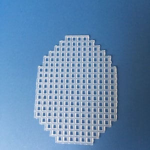 May include: A clear, egg-shaped plastic canvas sheet with a grid of square holes. The craft supply is designed for needlepoint or cross-stitch projects. The sheet is on a blue background.