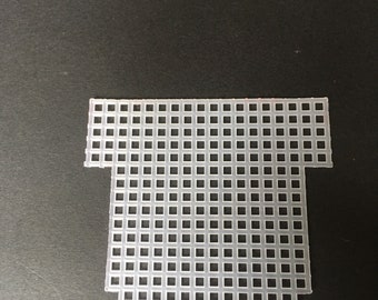 May include: A translucent, off-white plastic canvas sheet with a grid of square holes. The sheet is shaped like a stylized T-shirt, with a rectangular body and a shorter, wider top section. The edges are clean-cut.