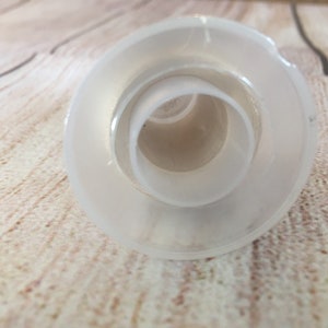 K&ouml;nnte beinhalten: Ein klarer, mattierter Glasflaschenverschluss mit kreisf&ouml;rmigem Design. Der Verschluss hat eine breite, flache Basis und eine Reihe konzentrischer Ringe, die sich zur Mitte hin verj&uuml;ngen. Das Objekt besteht aus Glas und ist f&uuml;r die &Ouml;ffnung einer Flasche bestimmt.