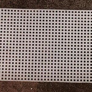 Op de afbeelding: Een rechthoekig stuk wit plastic canvas met een raster van vierkante gaten. De randen zijn ongelijkmatig, met een gekarteld patroon aan één kant. Geschikt voor borduurwerk en kruissteekprojecten.