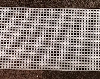 Könnte beinhalten: Ein rechteckiges Stück weißes Kunststoff-Canvas mit einem Gitter aus quadratischen Löchern. Die Kanten sind unregelmäßig, mit einem gezackten Muster auf einer Seite. Für Nadelarbeiten wie Kreuzstich geeignet.