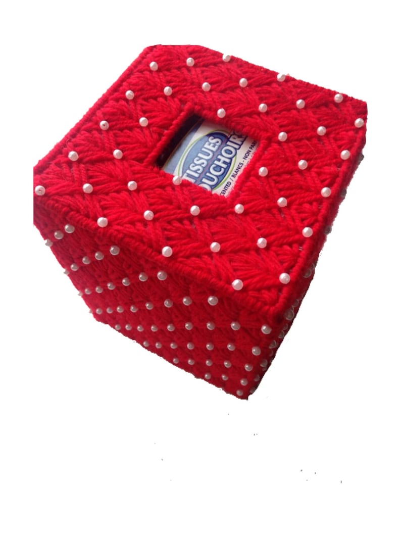 Op de afbeelding: Een rode, handgemaakte tissuebox cover. De cover is gemaakt van rood garen en versierd met kleine, witte parel kralen. De tissuebox heeft een vierkante opening voor het afgeven van tissues. De tekst "TISSUES DUCHOIR" is zichtbaar.