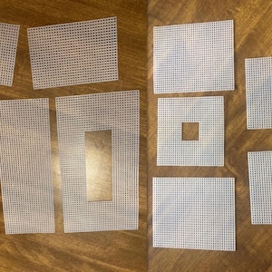 May include: A collection of white plastic canvas pieces in various shapes and sizes. The pieces include rectangles, squares, and shapes with cut-out sections. The canvas has a grid-like pattern, suitable for needlepoint or cross-stitch projects.
