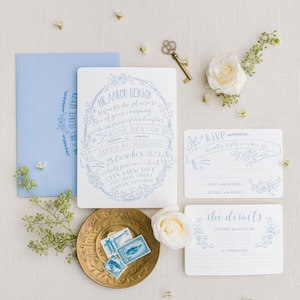 May include: A wedding invitation suite with a blue and white floral design. The invitation card features the text "Mr. Aaron Benson requests the pleasure of your company at the marriage of his daughter Katie Benson to Mr. Jared Richardson 28 October 2023 at half past one o'clock City View Loft 725 State Street Madison, Wisconsin". The RSVP card features the text "RSVP kindly reply by October 15th Accept with pleasure Declines with regrets". The details card features the text "The details Ceremony and Reception Accommodations".