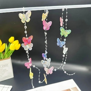 May include: Three hanging strands of iridescent butterfly ornaments made of translucent plastic. Each strand features multiple butterflies in various colours including yellow, pink, blue, and clear, interspersed with small clear beads on thin wire.