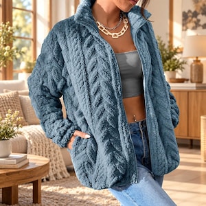 May include: A blue zip-up jacket made of a textured, fuzzy fleece material with a prominent herringbone pattern. The jacket features a high collar, long sleeves, and two side pockets. It is worn over a gray tube top and light blue denim jeans.