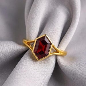 Anello in oro con granato rosso intenso taglio esagonale incastonato a castone e gambo diviso, fede nuziale geometrica minimalista, gioiello di lusso da regalare.