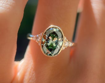 Bague de fiançailles en or massif orné d'un diamant ovale vert, serti clos et entouré de diamants. Bague d'exception, bague de demande en mariage.