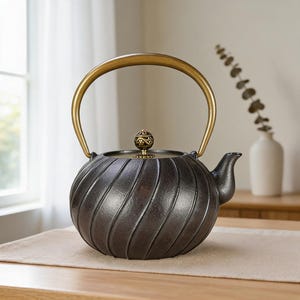 May include: A dark grey cast iron teapot with a textured, spiralling ribbed surface. It features a tall, arched brass-coloured handle and a matching lid knob with intricate filigree detailing. The spout is short and curved, extending from the side.