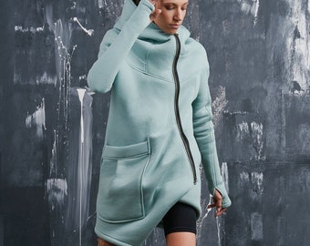 May include: A light blue hooded sweatshirt with a long zipper and a large pocket on the front. The sweatshirt is styled with black shorts and black high-top sneakers.