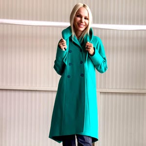May include: A teal double-breasted coat with a wide collar and a flared silhouette. The coat features large, matching buttons and is worn with dark blue jeans and sneakers. The coat's length extends to the mid-calf.